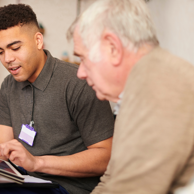 Person Visiting Older Man In His Home Completing Something On An Ipad